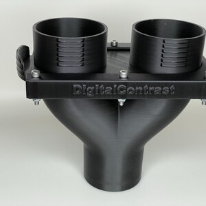 May include: A black 3D-printed object with two cylindrical openings and a Y-shaped base. The object has the text "DigitalContrast" on the top surface and is secured with multiple screws. The design appears to be a custom-made component.