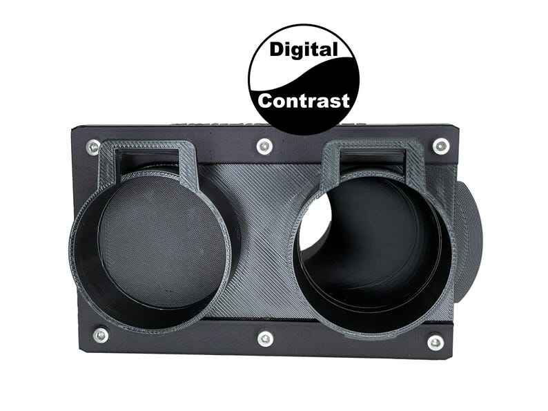 May include: A black, rectangular device with two circular openings and a textured surface. The device has a handle above each opening and is secured with silver screws. The text "Digital Contrast" is displayed above the device.