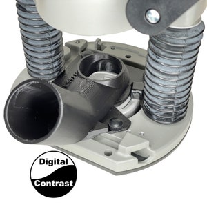 May include: A close-up of a router base with a black dust collection port and a gray base. The base has a black knob and a silver ring. The base is attached to a black dust collection hose.