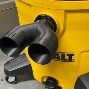 May include: A black, Y-shaped vacuum hose attachment is connected to a bright yellow DEWALT vacuum cleaner. The attachment has two openings and is made of a 3D-printed material. The vacuum cleaner has a black base with wheels.
