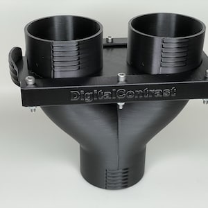 May include: Black 3D-printed plastic component with two cylindrical openings and a funnel-shaped base. The component has a rectangular top with the text "DigitalContrast" and is secured with screws. The design suggests a functional, possibly industrial, product.