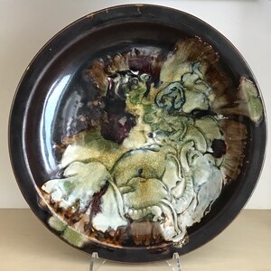 May include: A ceramic plate with a dark brown glaze and a raised design of green, white, and brown floral patterns.