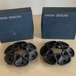 Könnte beinhalten: Zwei schwarze Boxen mit dem Text "DANSK DESIGNS" auf der Vorderseite. Zwei schwarze Kerzenhalter aus Metall mit einem runden Design.