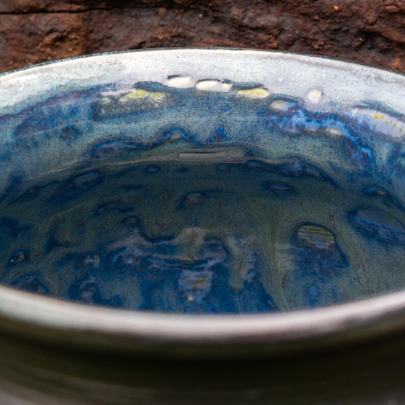May include: A ceramic bowl featuring a glossy, multi-tonal glaze with deep blue, light blue, and hints of white and yellow. The interior surface displays a fluid, marbled pattern with varying shades of blue, creating a smooth, reflective finish.