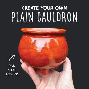May include: A glossy orange ceramic cauldron with a rounded body and three small feet. The text above reads CREATE YOUR OWN PLAIN CAULDRON, and an arrow points to the text PICK YOUR COLORS on the left side against a dark background.