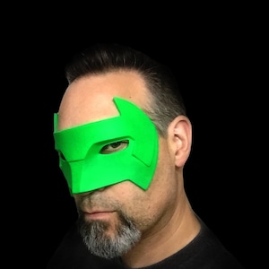 May include: A person wearing a green superhero mask with a pointed top and a dark gray beard.