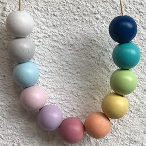 May include: A string of wooden beads in pastel colors, including light blue, pink, lavender, and yellow. The beads are strung on a white cord.