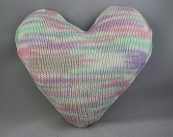 May include: A heart-shaped knitted pillow with a striped pattern in shades of pink, green, and purple.