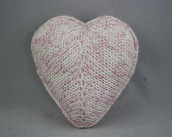 May include: A heart-shaped knitted pillow with a white and pink yarn pattern.