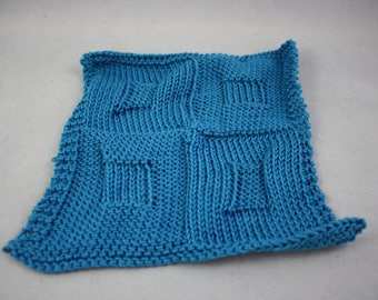 May include: A square, knitted teal washcloth with a textured pattern. The washcloth is divided into four sections, each with a different stitch pattern. The edges are neatly finished, and the overall appearance is handmade.