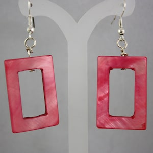 May include: A pair of pink rectangular earrings with a silver hook closure. The earrings are made of a material that has a pearlescent finish.