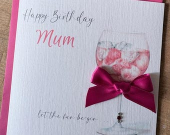 May include: A square greeting card with a white textured background featuring the text Happy Birthday Mum in black and pink script. An illustration of a glass filled with pink liquid and ice is adorned with a bright pink satin ribbon bow.