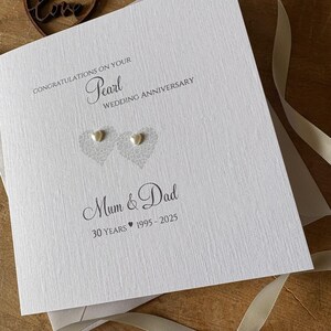 May include: A white Pearl Wedding Anniversary card with the text "Congratulations on your Pearl Wedding Anniversary" and "Mum & Dad". The card features two heart-shaped designs with pearl embellishments and the text "30 Years 1995-2025".