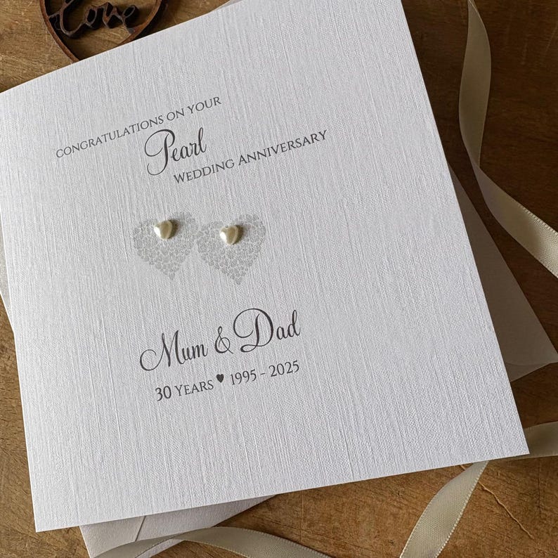 May include: A white Pearl Wedding Anniversary card with the text "Congratulations on your Pearl Wedding Anniversary" and "Mum & Dad". The card features two heart-shaped designs with pearl embellishments and the text "30 Years 1995-2025".