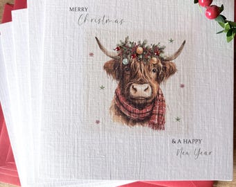 May include: A square greeting card with a textured white finish featuring a brown Highland cow wearing a red plaid scarf and a festive wreath on its horns. The text reads Merry Christmas and & A Happy New Year in black script and serif fonts.