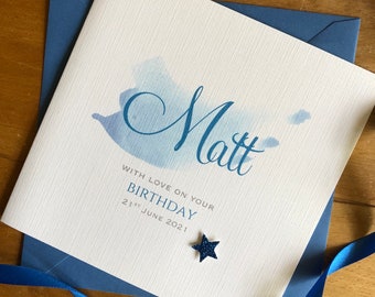 May include: A blue and white birthday card with the name "Matt" written in cursive. The card has a watercolor design and the text "With love on your birthday 21st June 2021".
