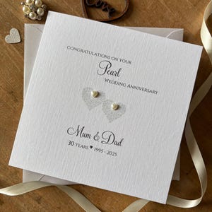 May include: A white Pearl Wedding Anniversary card with the text "Congratulations on your Pearl Wedding Anniversary" and "Mum & Dad 30 Years 1995-2025". The card features two heart-shaped designs with pearl embellishments.
