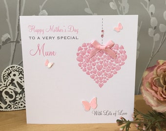May include: A pink and white card with the text "Happy Mother's Day to a very special Mum" and a pink heart made of smaller hearts. The card also has a pink bow and butterflies.