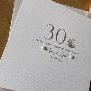 May include: A white textured anniversary card with the number "30" and the text "Happy Pearl Wedding Anniversary". The card includes the words "Mum & Dad" and the years "1995 2025". Two pearl embellishments are visible.
