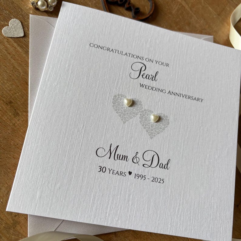 May include: A white Pearl Wedding Anniversary card with the text "Congratulations on your Pearl Wedding Anniversary" and "Mum & Dad 30 Years 1995-2025". The card features two heart-shaped designs with pearl embellishments.