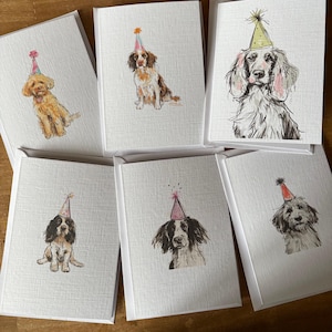 May include: Six greeting cards with dog illustrations wearing party hats. The dogs are depicted in watercolour, with different breeds and colours. The cards are set against a textured white background and come with white envelopes.