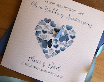 May include: A white card with blue text that reads "Congratulations on your China Wedding Anniversary." A blue heart made of smaller hearts is in the center of the card. The text "Mum & Dad" is below the heart with the text "20 YEARS 12th MARCH 2002 - 2022" below that.