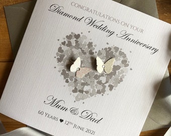 May include: A white card with a gray heart design and two white butterflies. The card says "Congratulations on your Diamond Wedding Anniversary" and "Mum & Dad 60 Years 12th June 2021".