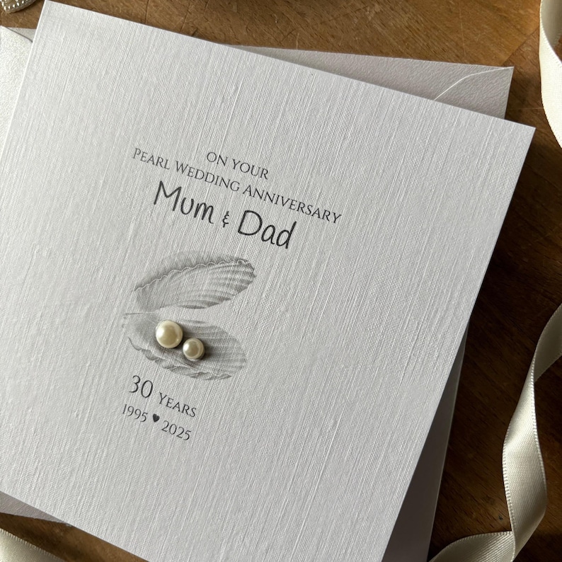 May include: A light gray Pearl Wedding Anniversary card with the text "On Your Pearl Wedding Anniversary Mum & Dad". The card features an illustration of an open oyster shell with two pearls and the text "30 Years 1995-2025".