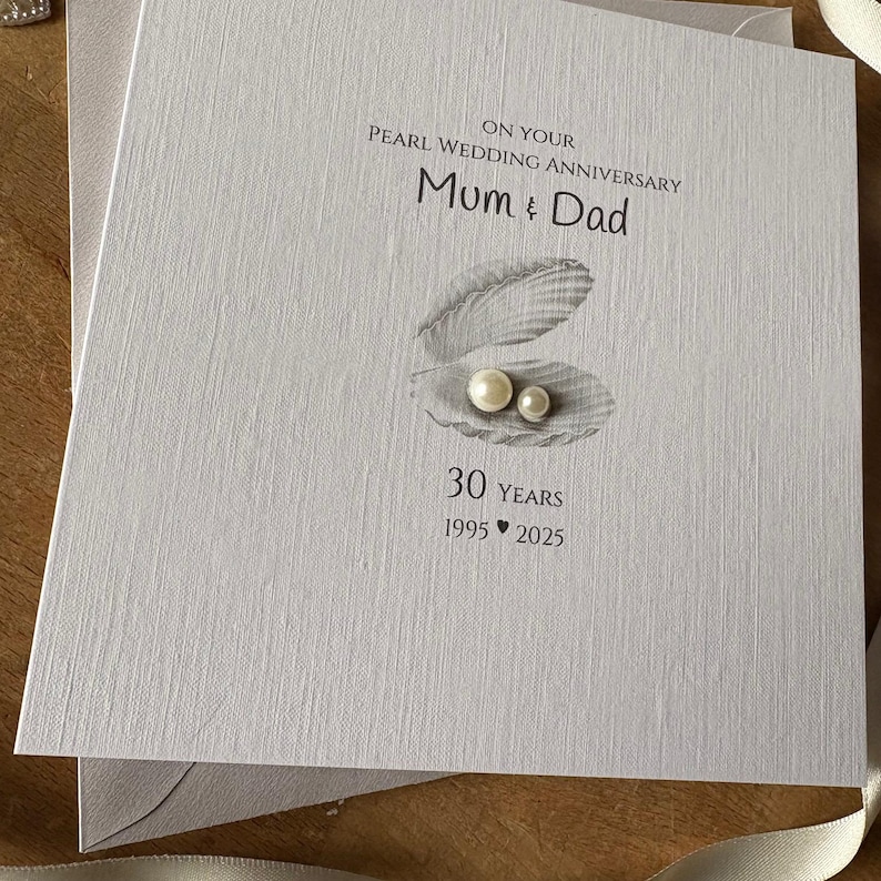 May include: A light gray Pearl Wedding Anniversary card with the text "On Your Pearl Wedding Anniversary Mum & Dad". The card features an illustration of a shell with two pearls and the text "30 YEARS 1995 2025".