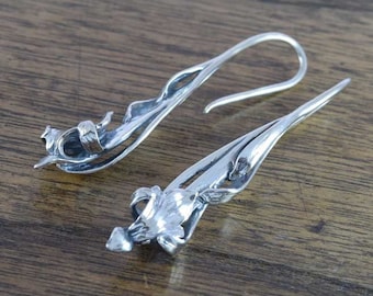 May include: A pair of silver dangle earrings featuring a delicate flower design. The earrings are made of sterling silver and have a hook closure.