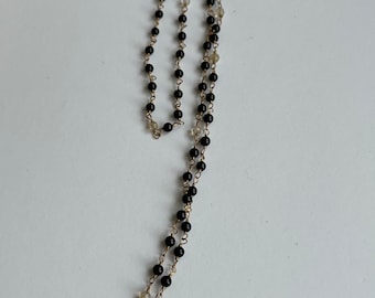 May include: A gold necklace with black and clear beads and a gold charm with the word "Queen" and a small crescent moon charm.