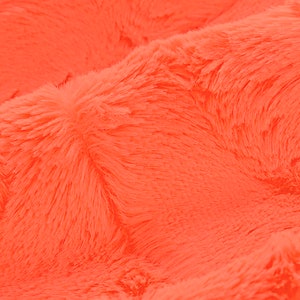 May include: Close-up of a bright orange fluffy fabric. The fabric has a soft, plush texture.