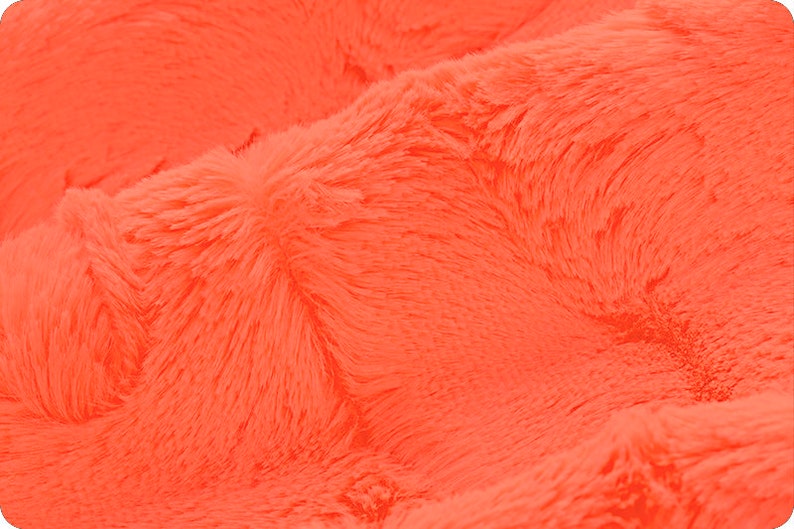 May include: Close-up of a bright orange fluffy fabric. The fabric has a soft, plush texture.