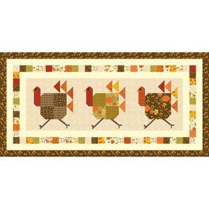 May include: A rectangular quilt featuring three stylized turkeys in patchwork. The turkeys have red wattles, and their bodies are made of various patterned fabrics in shades of brown, orange, and green. The quilt is bordered with autumn-themed patterns.
