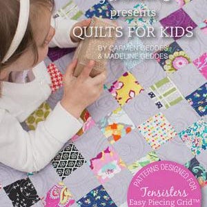 May include: A colorful quilt with a patchwork design, featuring squares of various patterns and colors. The quilt is the focus, with a child holding a small object. The text on the quilt reads "QUILTS FOR KIDS" and "Tensisters".