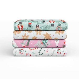 May include: A stack of four folded sheets with festive Christmas patterns. The top sheet is light blue with nutcrackers and pine branches. The second sheet is white with gingerbread men. The third sheet is pink with llamas. The bottom sheet is white with candy canes.