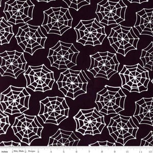 May include: Dark purple fabric with a repeating pattern of white spiderwebs. The spiderwebs are evenly spaced and vary slightly in size. The fabric is marked with inches along the bottom edge.