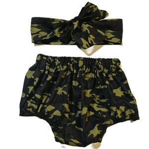 Könnte beinhalten: Ein Baby-Outfit in Tarnmuster-Druck in Schwarz und Grün mit einem Stirnband und einer Latzhose.