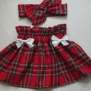 May include: Red and black tartan skirt with white bows on the sides. The skirt is made from a soft, comfortable fabric and has a gathered waistband. It is perfect for a little girl's special occasion.