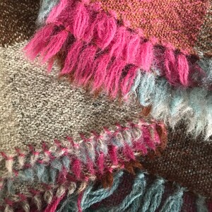 May include: A multi-colored knitted throw blanket with fringe. The blanket is made of a soft, fuzzy yarn in shades of brown, pink, and blue.