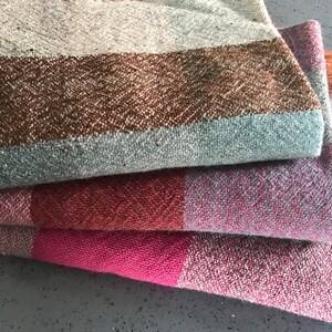 May include: A stack of four woven blankets in various shades of brown, pink, and gray. The blankets have a textured, woven pattern and are folded neatly.