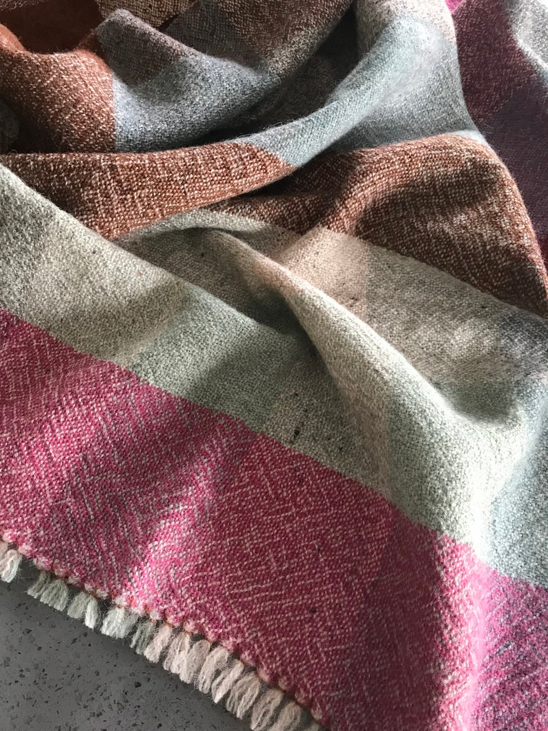 May include: A woven throw blanket with a fringe border. The blanket is made of a soft, textured fabric and features a striped pattern in shades of brown, gray, and pink.