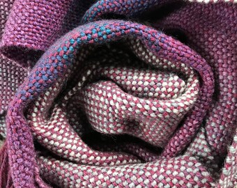 May include: A pink and white woven scarf with a fringe. The scarf is rolled up and the fringe is visible.