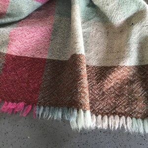 May include: A woven throw blanket with a brown, pink, and gray plaid pattern. The blanket has a fringe border.