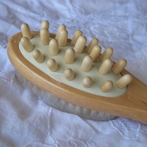 Op de afbeelding: Een houten lichaamsborstel met een lichtbruine handgreep en een witte borstel met borstels. De borstel heeft een rij houten knoppen aan de bovenkant.
