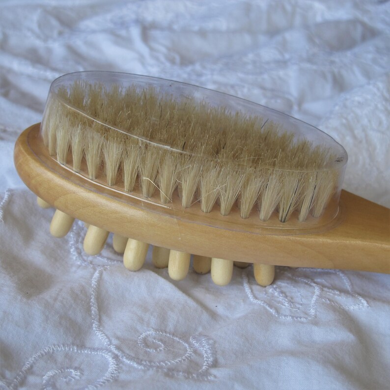 Op de afbeelding: Een houten lichaamsborstel met natuurlijke haren en een transparante plastic hoes. De borstel heeft een rij houten knoppen aan de achterkant.