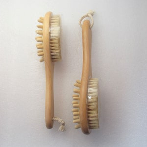 Op de afbeelding: Twee houten lichaamsborstels met natuurlijke borstels. Elke borstel heeft een lange houten handgreep en een rond borstelhoofd met zowel zachte als stevige borstels.