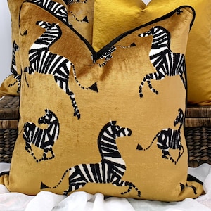 May include: Mustard yellow decorative throw pillows with a zebra pattern. The pillows have a black border and a soft, textured appearance. The zebra design is black and white, with the zebras in various poses.