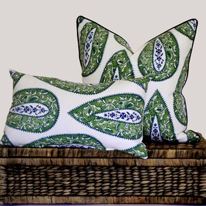 May include: Two decorative throw pillows with a white background and a green and blue paisley pattern. The pillows are sitting on a woven wicker basket.