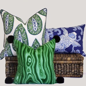 May include: Three decorative throw pillows with pom-poms. The pillows are on a woven wicker basket. The pillows are green, blue, and white with paisley and fish patterns.